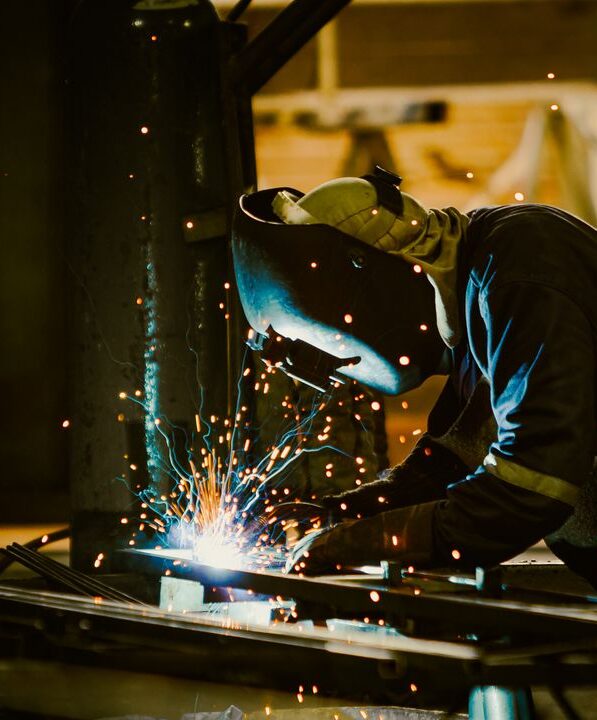 A welder in protective gear works in an industrial setting, with sparks illuminating the scene.